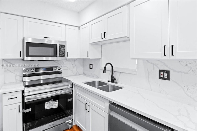 kitchen with tasteful backsplash, appliances with stainless steel finishes, white cabinetry, a sink, and light stone countertops