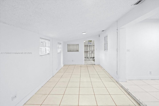 unfurnished room featuring light tile patterned floors, vaulted ceiling, and a textured ceiling