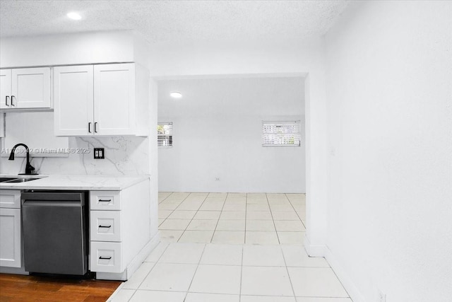 kitchen featuring a textured ceiling, dishwashing machine, a sink, and white cabinets