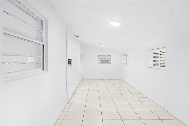 interior space with a textured ceiling, light tile patterned flooring, and vaulted ceiling