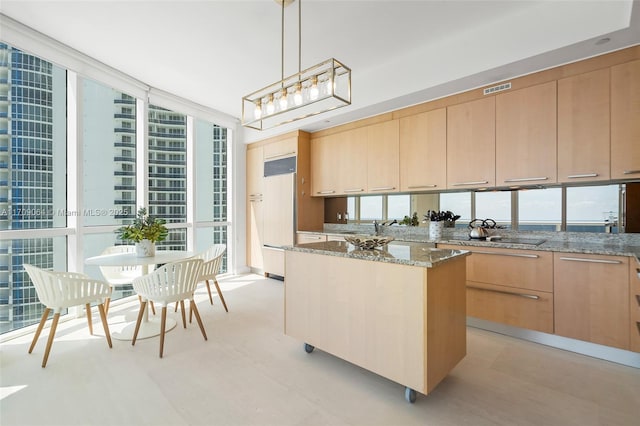 kitchen featuring light brown cabinets, pendant lighting, light stone counters, and a wall of windows