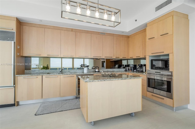 kitchen with light stone counters, a center island, built in appliances, and light brown cabinetry