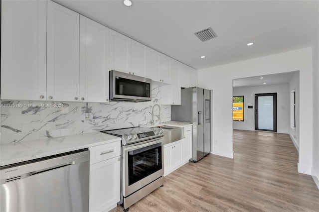 kitchen with decorative backsplash, light hardwood / wood-style flooring, white cabinets, and appliances with stainless steel finishes