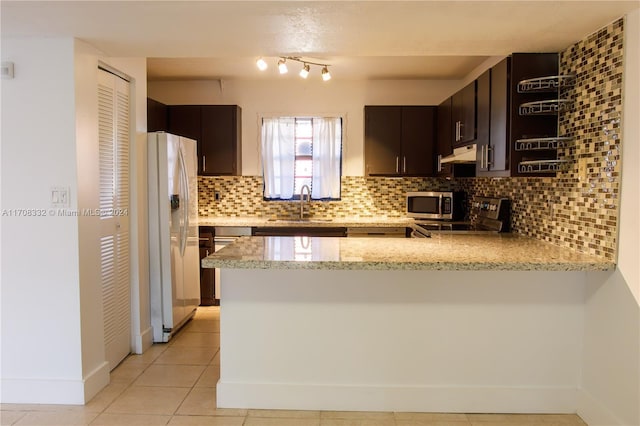 kitchen with backsplash, dark brown cabinets, light stone counters, kitchen peninsula, and stainless steel appliances