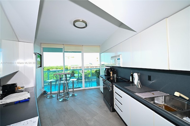 kitchen with white cabinetry, black electric range oven, and wood-type flooring