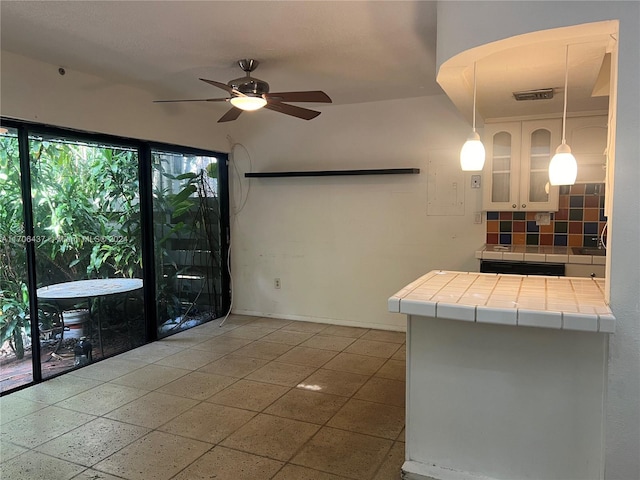 interior space featuring decorative backsplash, ceiling fan, tile countertops, white cabinetry, and hanging light fixtures