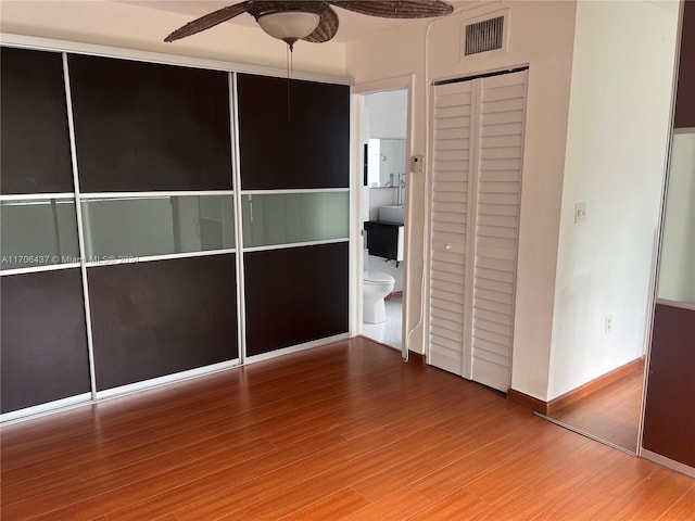 unfurnished bedroom featuring hardwood / wood-style flooring, ceiling fan, connected bathroom, and a closet