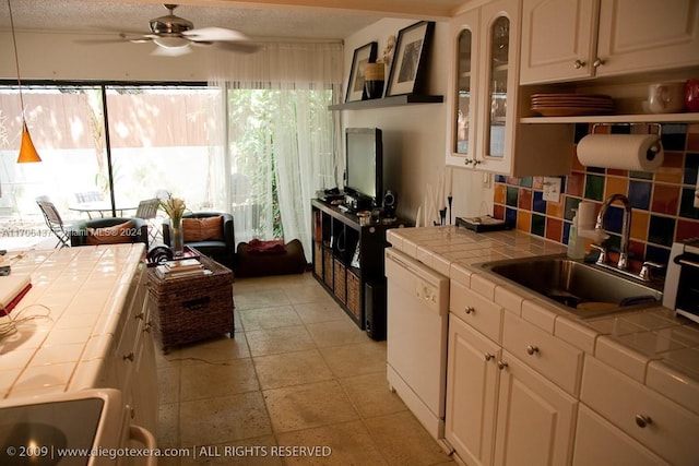 kitchen with tile countertops, dishwasher, white cabinetry, and sink