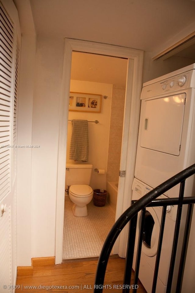 bathroom featuring toilet, a bathtub, stacked washing maching and dryer, and wood-type flooring