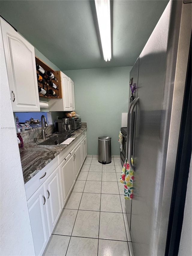 kitchen featuring sink, stainless steel fridge, white cabinetry, dark stone countertops, and light tile patterned flooring