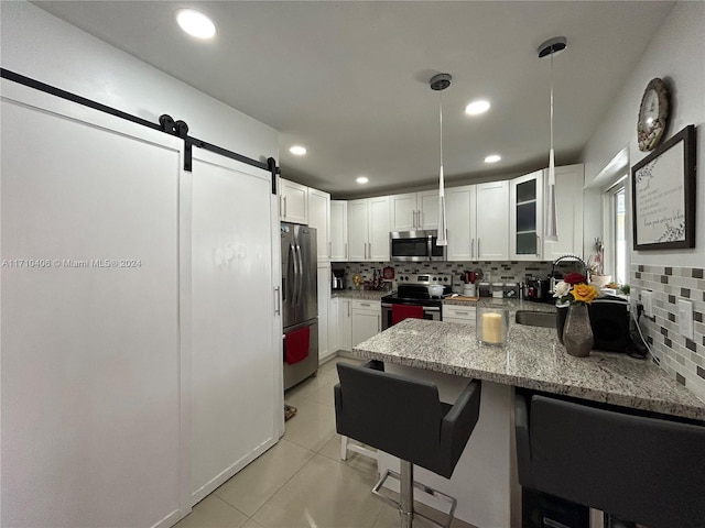 kitchen featuring tasteful backsplash, a barn door, decorative light fixtures, a breakfast bar, and appliances with stainless steel finishes