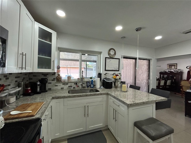 kitchen featuring light stone countertops, sink, hanging light fixtures, kitchen peninsula, and white cabinets