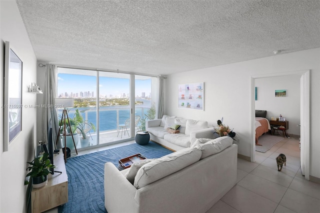 living room featuring a textured ceiling, a water view, expansive windows, and light tile patterned flooring