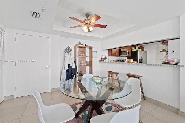 tiled dining space with ceiling fan, radiator, and a tray ceiling