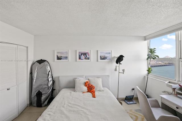 bedroom with a closet, a water view, a textured ceiling, and light tile patterned floors