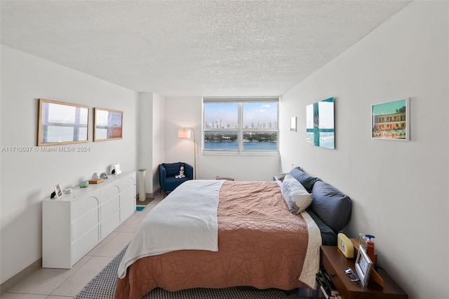 bedroom featuring multiple windows, light tile patterned floors, a water view, and a textured ceiling