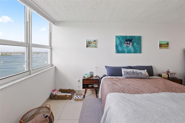 tiled bedroom featuring a textured ceiling, a water view, and multiple windows