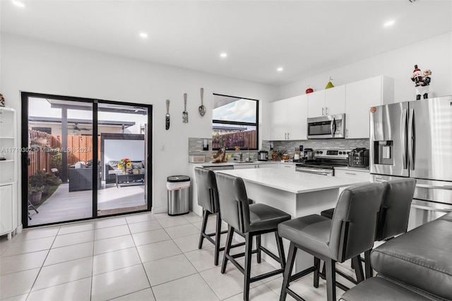 kitchen featuring decorative backsplash, appliances with stainless steel finishes, white cabinetry, a kitchen island, and a breakfast bar area