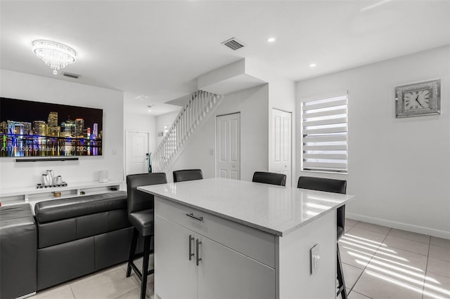 kitchen featuring a center island, white cabinets, light tile patterned floors, a notable chandelier, and a breakfast bar area