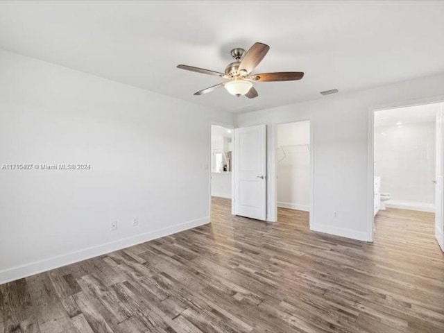 unfurnished bedroom featuring hardwood / wood-style floors, a closet, a spacious closet, and ceiling fan