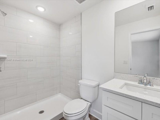 bathroom with tiled shower, vanity, and toilet