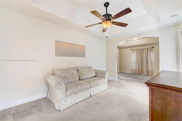 carpeted living room with ceiling fan and a raised ceiling