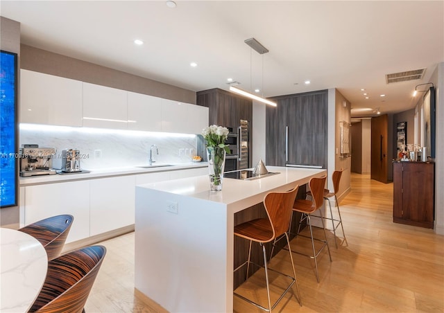 kitchen featuring decorative backsplash, decorative light fixtures, a center island with sink, light hardwood / wood-style flooring, and white cabinetry