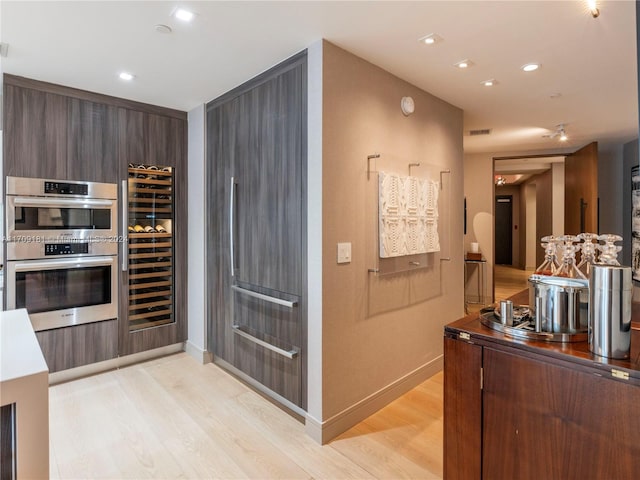 kitchen with double oven, light hardwood / wood-style flooring, beverage cooler, and dark brown cabinets