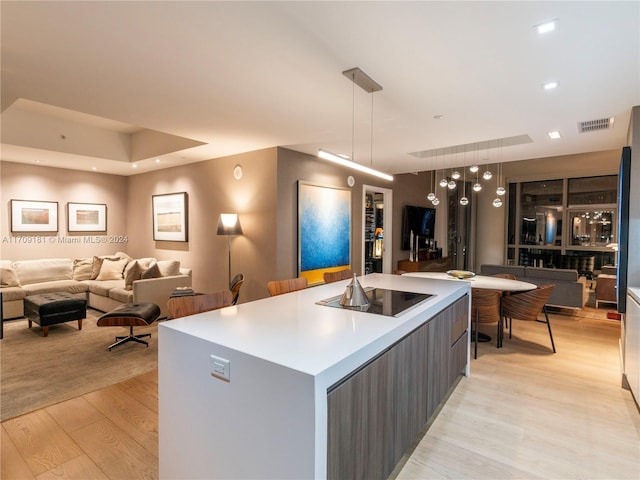 kitchen featuring pendant lighting, light wood-type flooring, a kitchen island with sink, and black electric cooktop