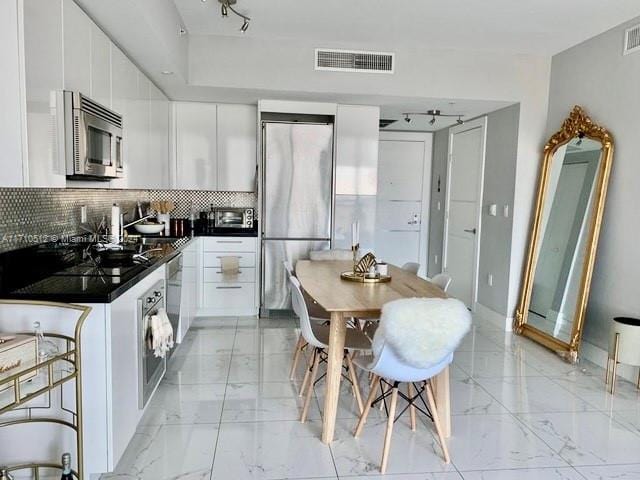 kitchen with white cabinets, rail lighting, stainless steel appliances, and backsplash