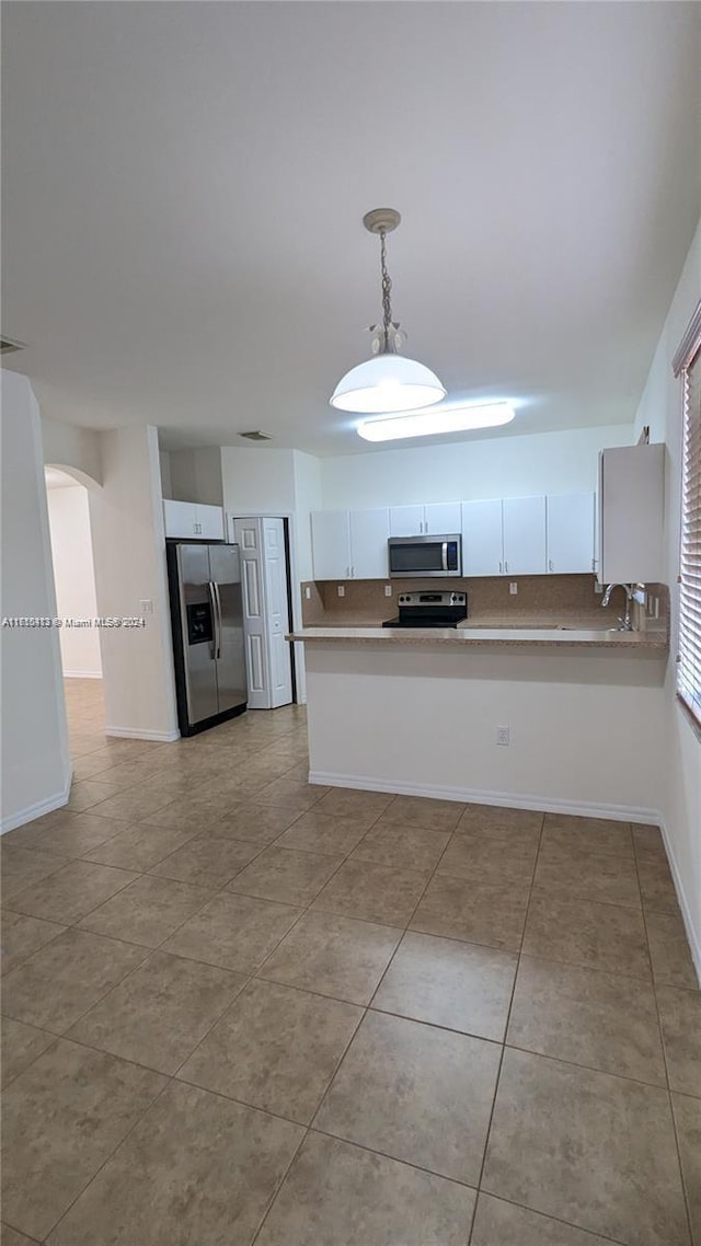 kitchen featuring kitchen peninsula, stainless steel appliances, pendant lighting, light tile patterned floors, and white cabinetry