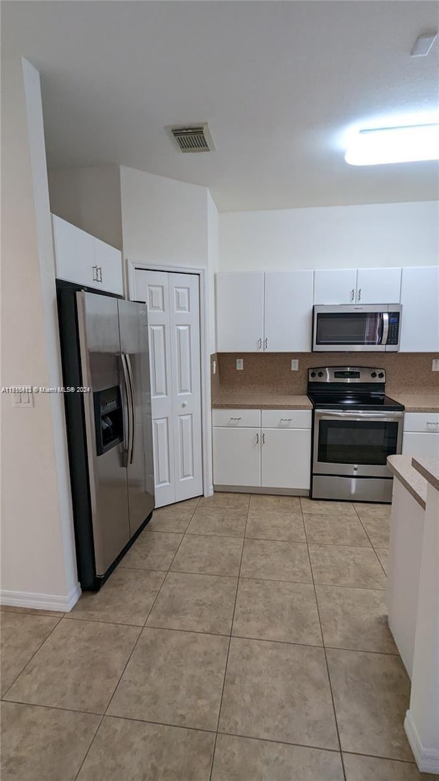 kitchen with appliances with stainless steel finishes, light tile patterned floors, and white cabinetry