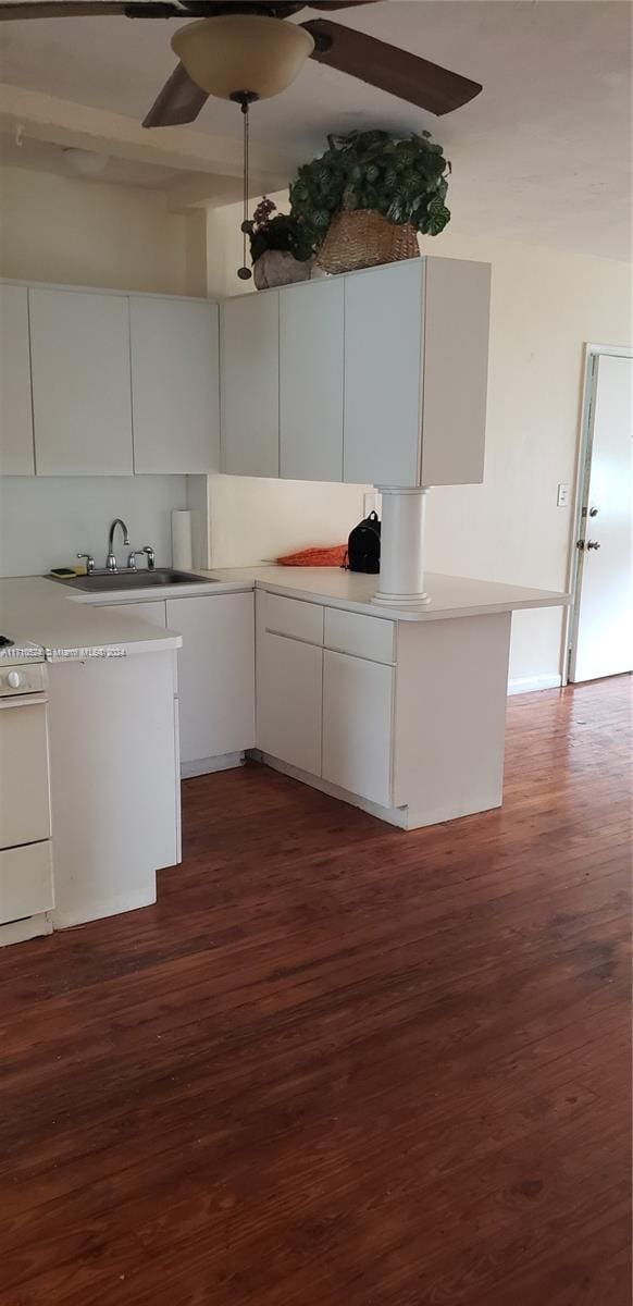 kitchen with white stove, dark wood-type flooring, ceiling fan, white cabinetry, and kitchen peninsula