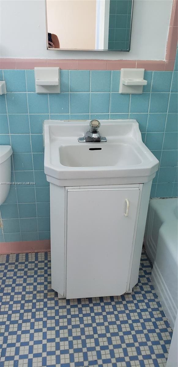 bathroom with vanity, a bath, toilet, and tile walls