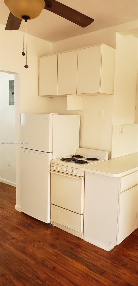 kitchen with white appliances, electric panel, dark hardwood / wood-style floors, decorative light fixtures, and white cabinetry