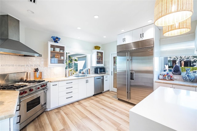 kitchen with white cabinetry, hanging light fixtures, wall chimney range hood, and premium appliances