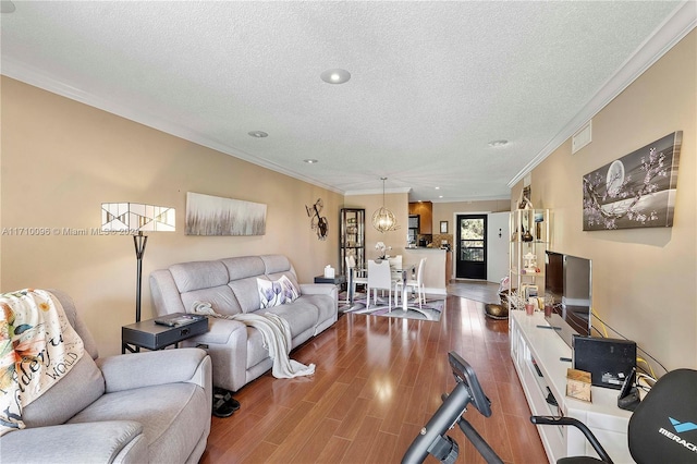 living room featuring hardwood / wood-style flooring, ornamental molding, a textured ceiling, and an inviting chandelier