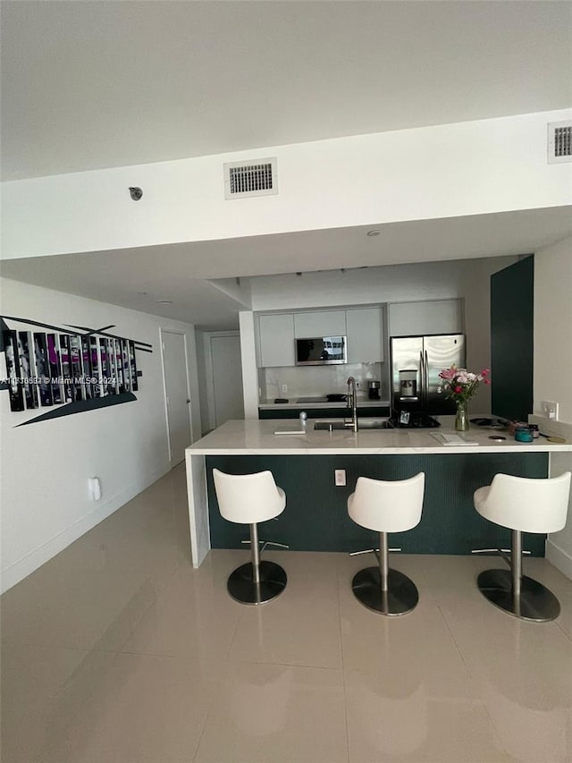 kitchen with stainless steel appliances, light tile patterned floors, kitchen peninsula, a breakfast bar area, and white cabinets