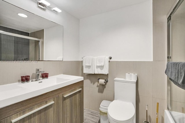 full bathroom featuring shower / bath combination with glass door, vanity, toilet, and tile walls