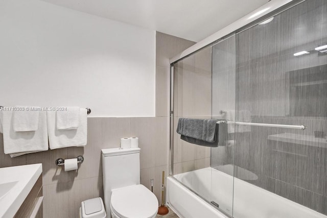 full bathroom featuring vanity, combined bath / shower with glass door, tile walls, and toilet