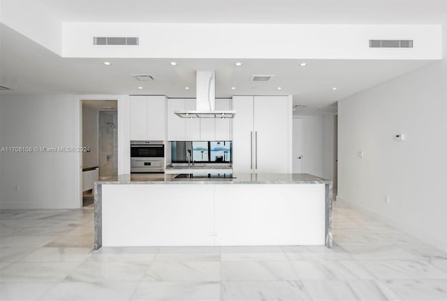 kitchen featuring light stone countertops, white cabinets, an island with sink, and custom range hood