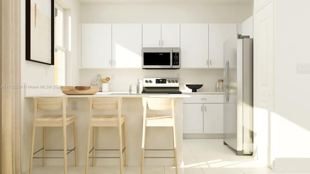 kitchen with white cabinetry, stainless steel appliances, a kitchen breakfast bar, and light tile patterned flooring