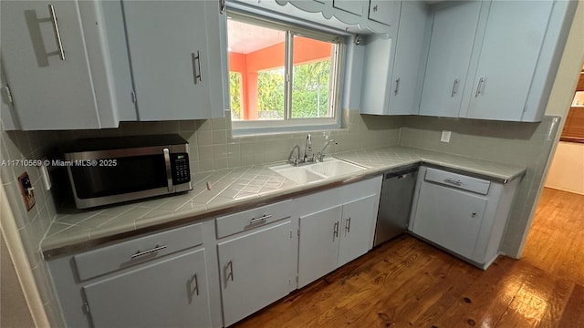 kitchen with sink, stainless steel appliances, hardwood / wood-style floors, decorative backsplash, and white cabinets