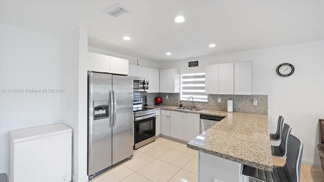 kitchen with sink, kitchen peninsula, decorative backsplash, appliances with stainless steel finishes, and white cabinetry