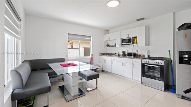 kitchen with appliances with stainless steel finishes, light tile patterned floors, white cabinetry, and sink