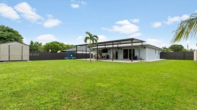 rear view of property with a patio, a trampoline, a shed, and a lawn