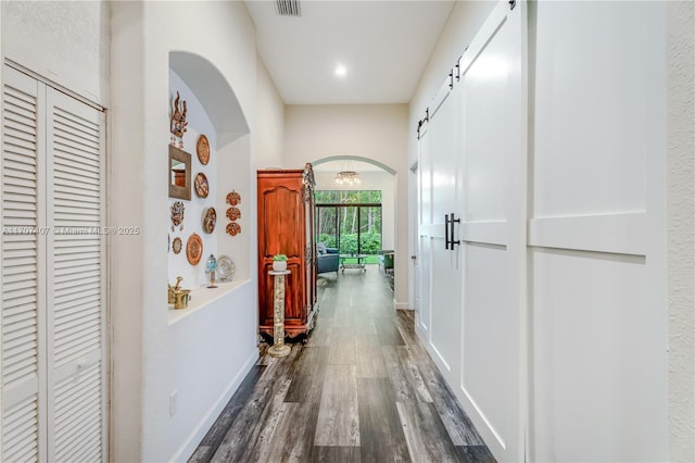 corridor with dark wood-type flooring, arched walkways, baseboards, and a barn door