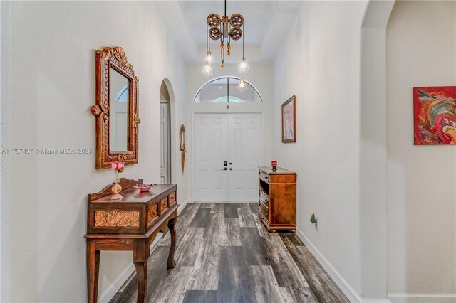 foyer featuring dark wood-style floors, baseboards, arched walkways, and a notable chandelier