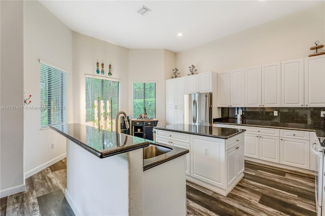 kitchen with freestanding refrigerator, tasteful backsplash, an island with sink, dark countertops, and dark wood finished floors