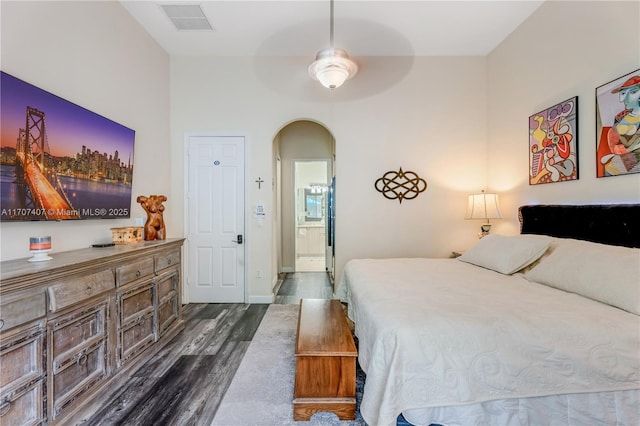 bedroom with visible vents, arched walkways, baseboards, ensuite bath, and dark wood-style flooring